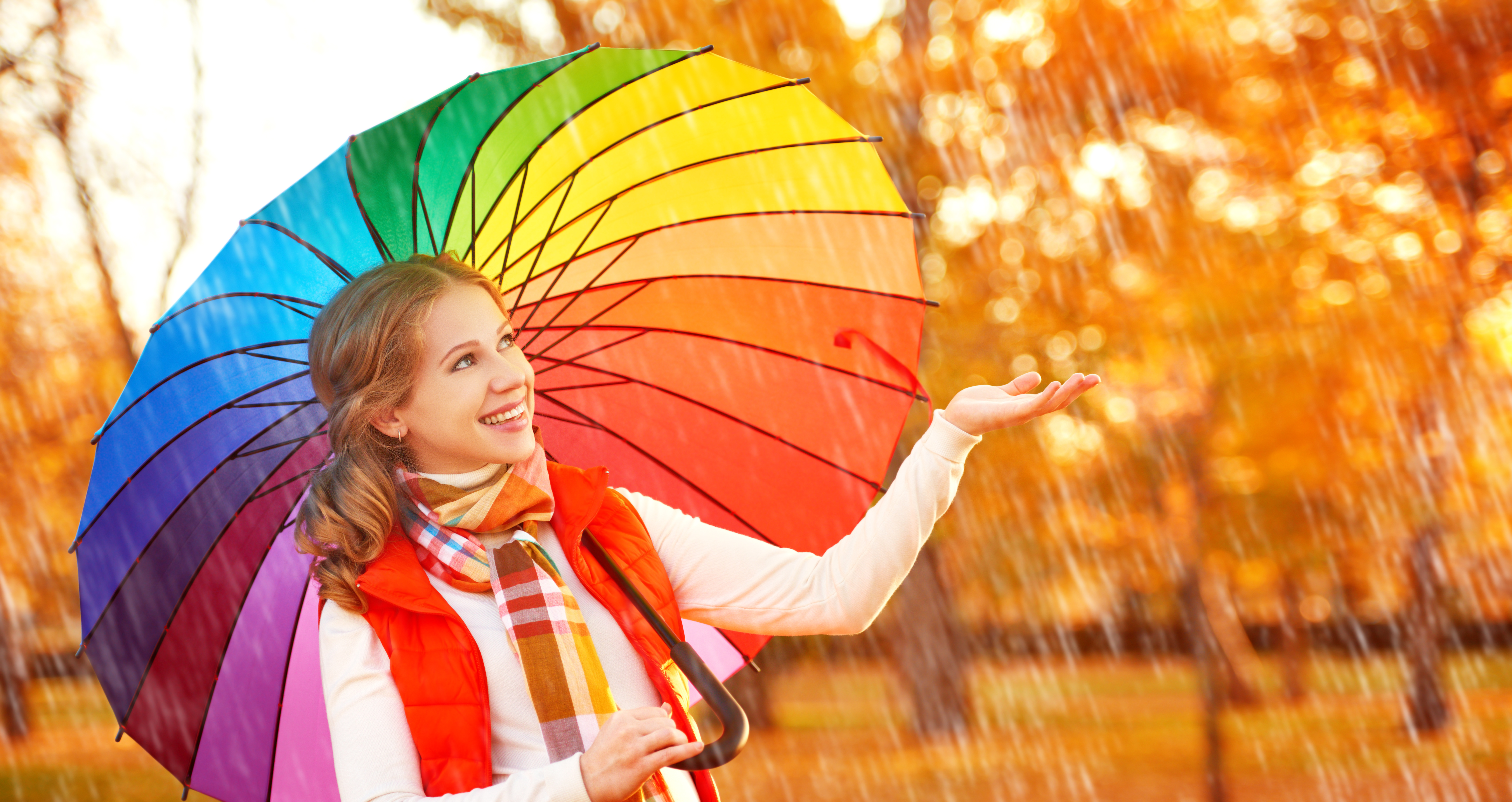 happy woman with rainbow multicolored umbrella under rain on nature in the park